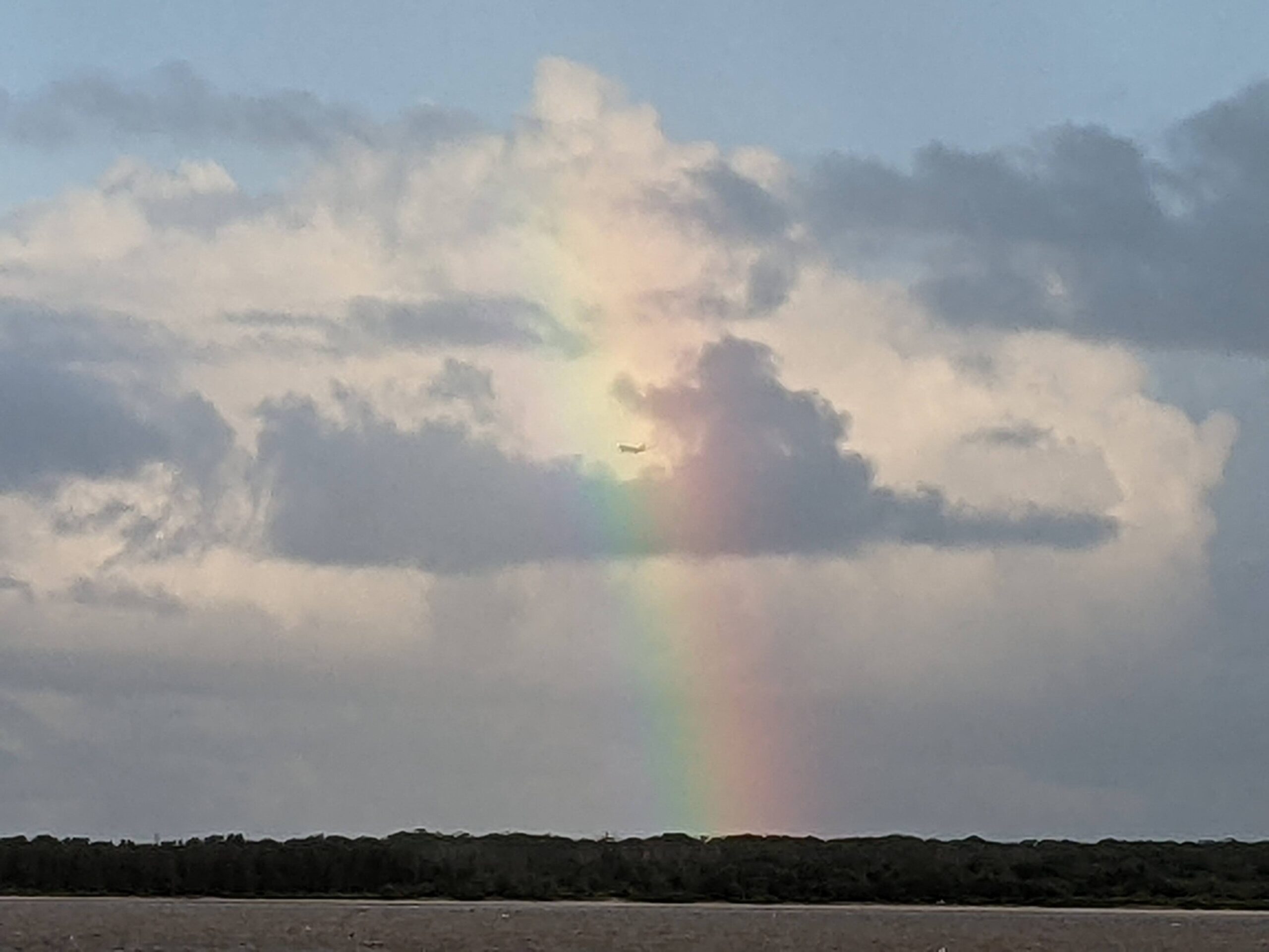 airplane flying through rainbow over nature reserve